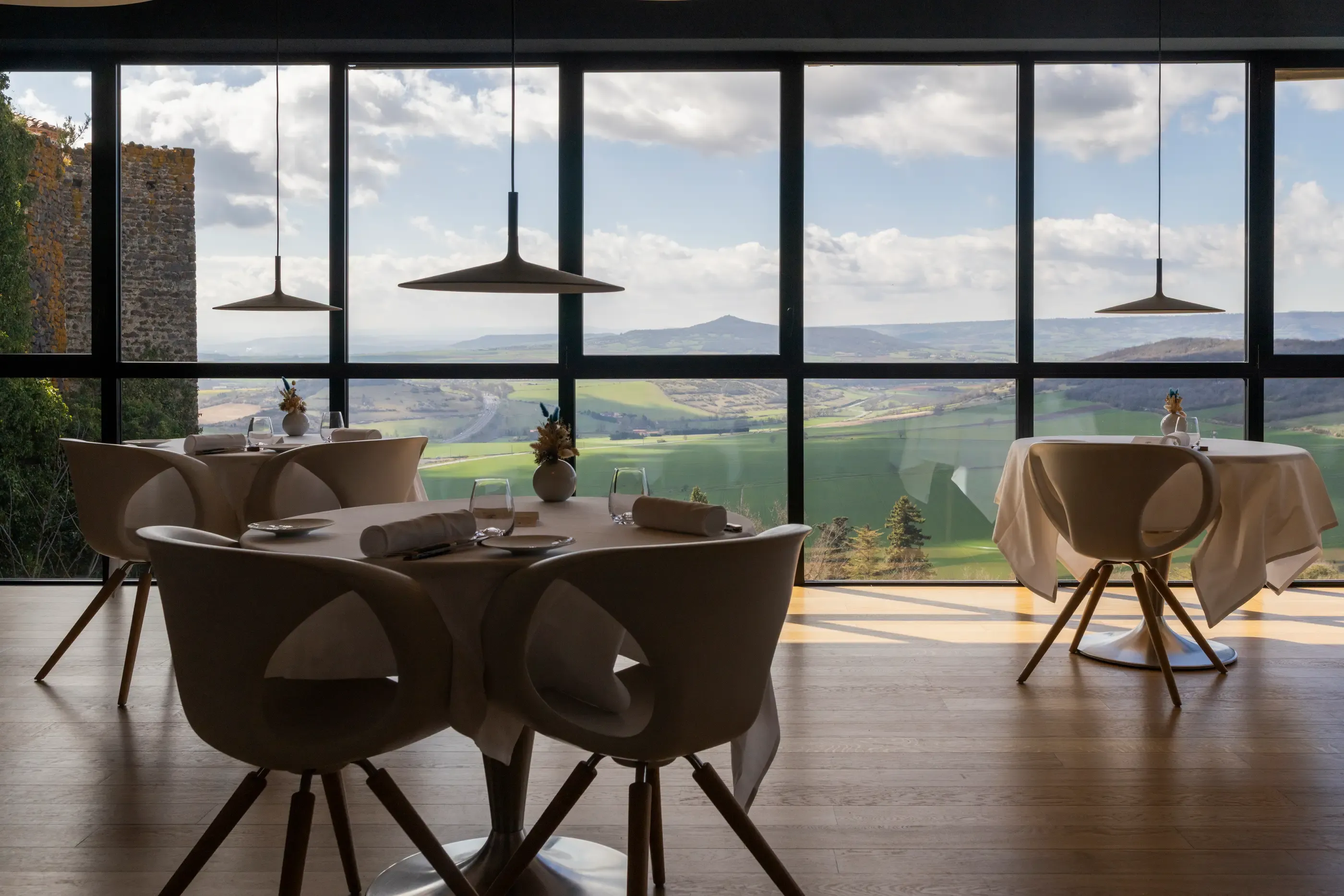 Une salle à manger avec une grande baie vitrée offrant une vue sur un paysage vallonné et des montagnes au loin