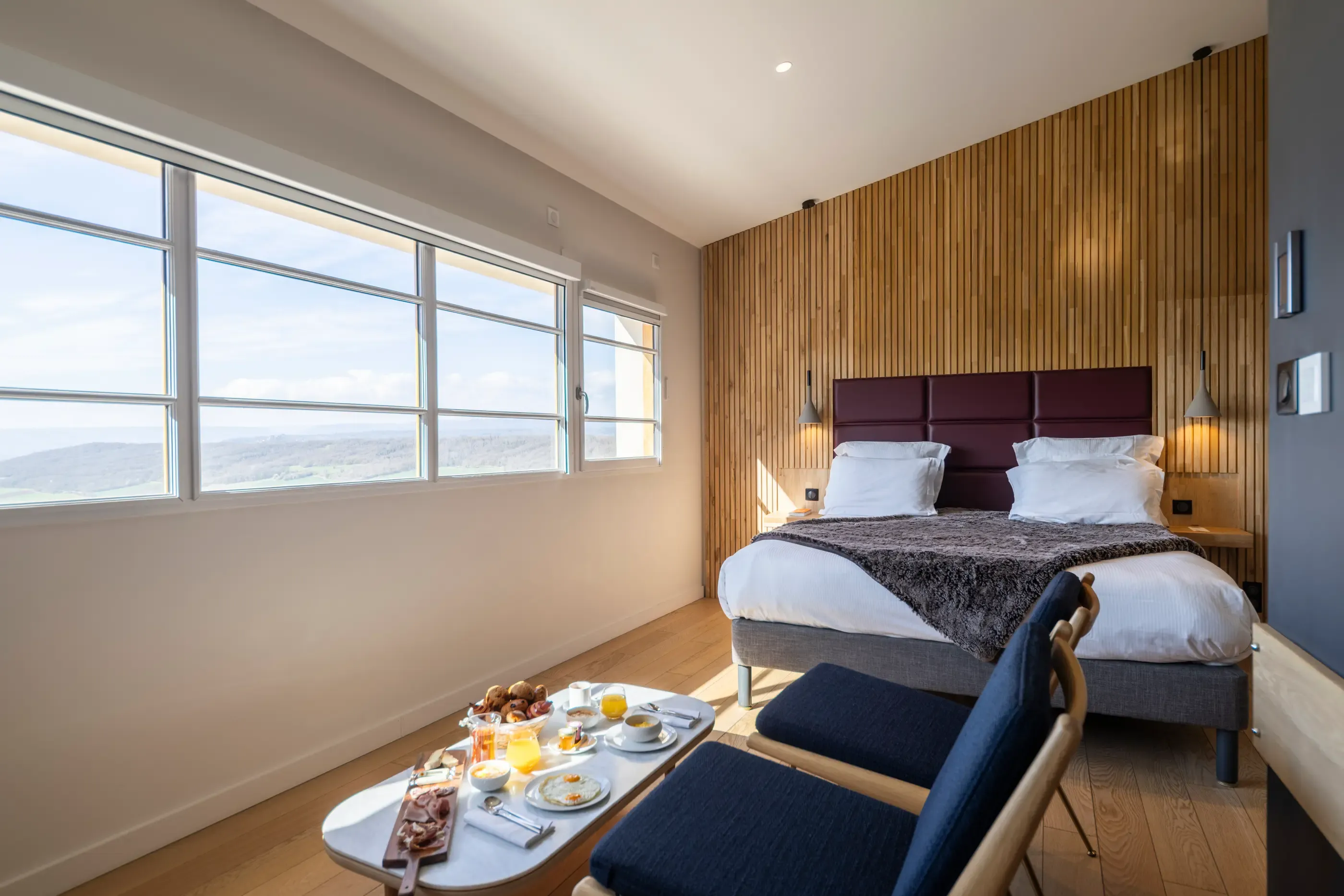 Chambre avec lit double, table avec petit-déjeuner et vue panoramique à travers de grandes fenêtres